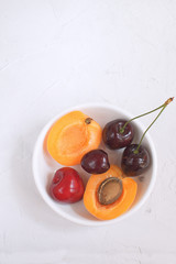 Apricots and cherries in white porcelain bowl Summer fruit and berries concept Harvesting Organic fruits White background Copy space