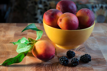 Ripe peaches in a yellow glass bowl on a wooden table. Blueberries and peaches with leaves lie in front of a yellow bowl. Fresh fruit for a healthy breakfast
