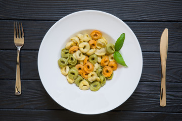Tortellini pasta with basil leaf on served table with fork and knife. Healthy italian cuisine on black wooden table background.