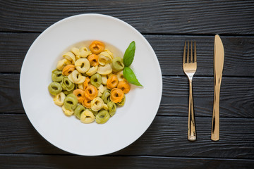 Tortellini pasta with basil leaf on served table with fork and knife. Healthy italian cuisine on black wooden table background.