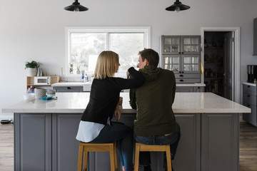 Rear view of couple sitting on stools in kitchen at home