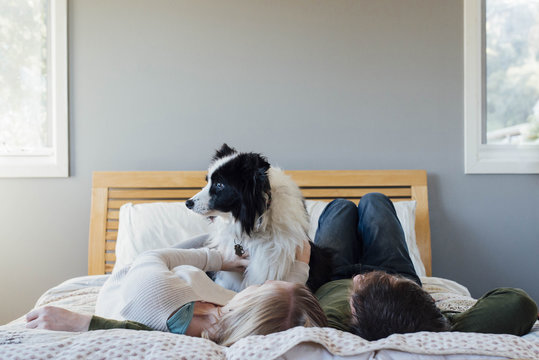 Couple With Dog Lying On Bed At Home