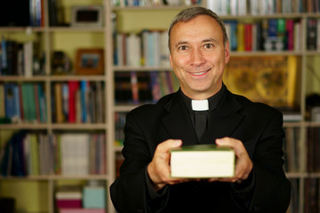 A good looking catholic priest is studying into his library. He looks at us with serenity, optimism...