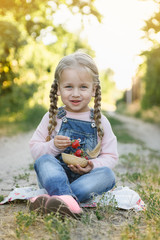 little girl is sitting on the grass and eating strawberries
