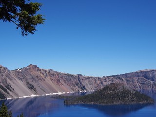 Fototapeta premium The magnificent rich blue waters of Crater Lake with reflections of the rim in the forests of Southern Oregon on a beautiful sunny summer morning. 