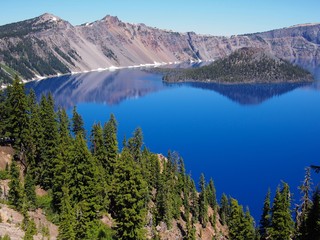Fototapeta na wymiar The magnificent rich blue waters of Crater Lake with reflections of the rim in the forests of Southern Oregon on a beautiful sunny summer morning. 