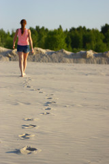 A young girl is seen from behind as she walks, leaving footprints in the sand