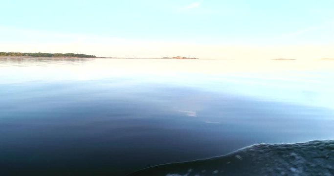 Dusk at Calm sea, C4K view of calm, clear and reflecting waters of the gulf of finland, from a boat, on a sunny summer evening sunset, in Hanko, Finland