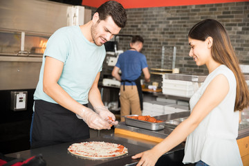 Handsome chef cooking pepperoni pizza and adding ingredients on top