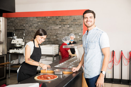 Smiling woman chef smearing tomato ketchup over pizza