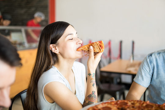 Beautiful young woman eating a slice of pizza in a restaurant