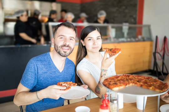 Handsome man with beautiful woman holding pizza slice looking at camera