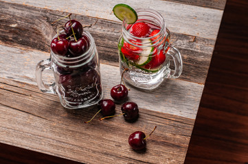 Fresh cherries and cup of water with fruit on wooden table.