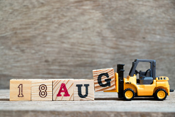 Toy forklift hold block G to complete word 18 aug on wood background (Concept for calendar date in...