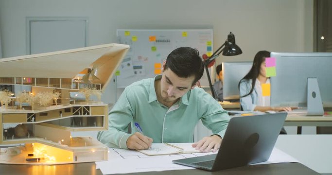 Young confident caucasian male architect working on an architectural model in the office at night.