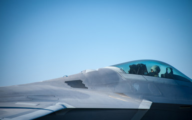 Fototapeta na wymiar A modern military jet fighter aircraft, grey against a blue sky with pilot visible in his helmet in the cockpit