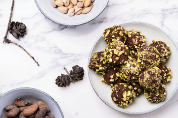 Homemade healthy vegan chocolate avocado truffles with pistachio in the bowl and ingredients and fir cones on grey marble table. Organic energy vegetarian sweet balls