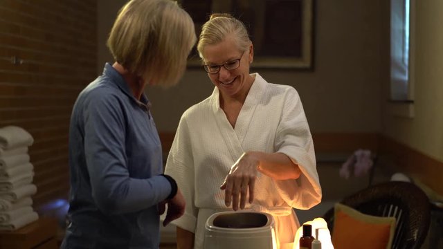 Camera sliding to the right of woman at a spa dipping her hands into hot paraffin for her skin treatment.