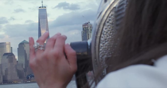 Close up of hand with engagement ring with New York City skyline in background.