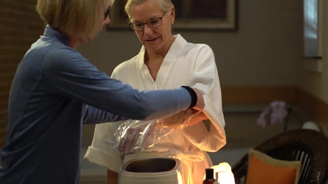 Pretty blonde woman takes her hand out of hot paraffin and an attendant at the spa puts her hand in a bag and glove.