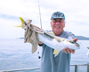 Happy mature senior caucasian tourist has caught a kingfish on a fishing charter boat at Doubtless...