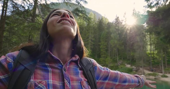 A beautiful woman while hiking, arrives at the destination after walking and exults from happiness for having achieved the goal.