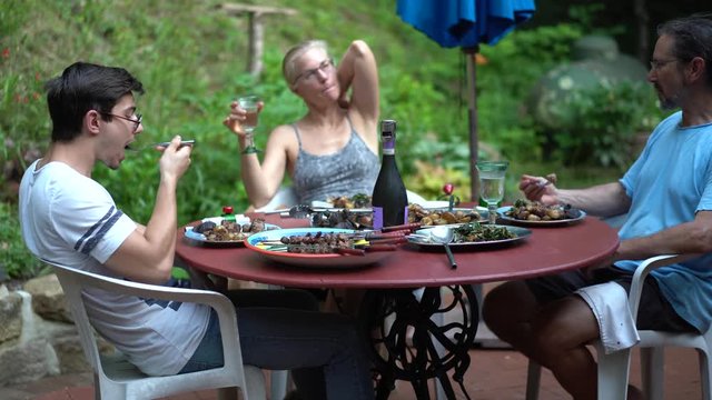 Family sitting around a table having dinner on an outdoor patio in a garden.
