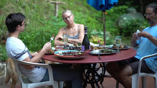 Family sitting around a table having dinner on an outdoor patio in a garden.