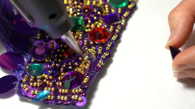 Extreme closeup of a finger pulling up, applying glue, and then pressing a large rhinestone into place for a belly dance costume.