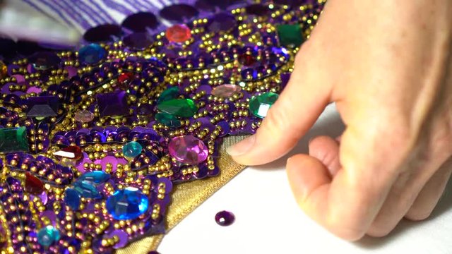 Extreme closeup of woman&rsquo;s finger pressing small round acrylic rhinestones into place with a glue gun.