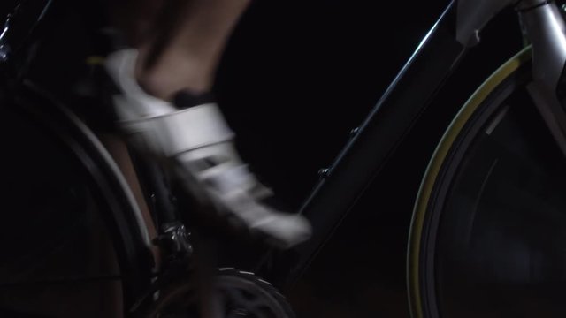 Tilt down of unrecognizable male cyclist riding bicycle against black background