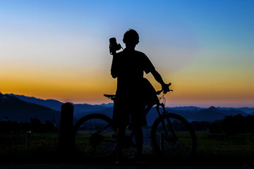 Obraz premium Silhouette of photographer in action take photo with bike on mountain with sunrise.