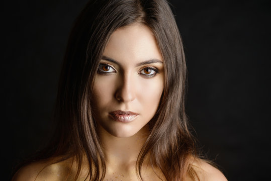 Close-up portrait of young woman with golden makeup.