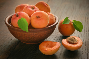 A brown bowl full of fruits of ripe apricot on a wooden table.