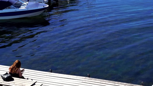 Girl reading a book in nice small docks with boats and yachts at sunny weather in Kjerringvik Norway