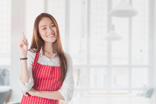 Portrait of Smiling beautiful young Asian woman wear red apron and hand pointing with copy space for your text or advertising isolated on blurred cafe background.