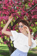 Attractive young woman posing near blossoming tree on sunny spring day