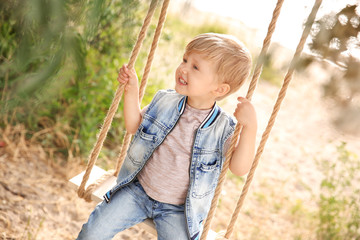 Cute little boy playing on swings in park