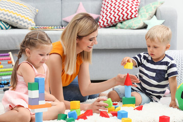 Young woman and cute children playing with constructor on floor at home