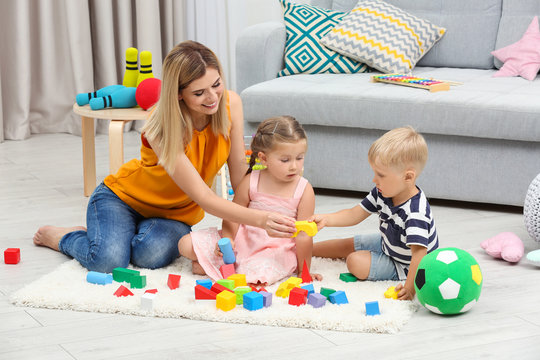 Young woman and cute children playing with constructor on floor at home