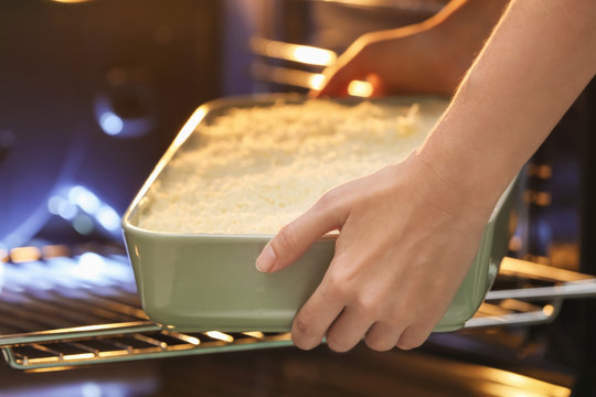 Woman putting baking dish with spinach lasagna into oven