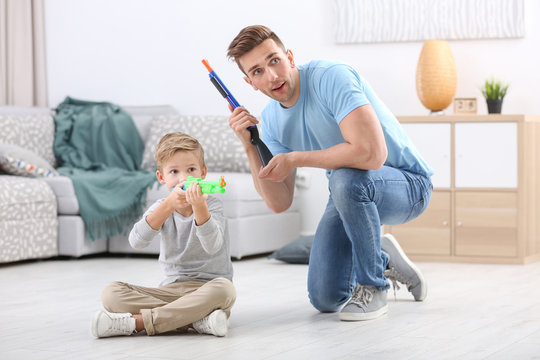 Cute boy and his father playing with toy guns at home