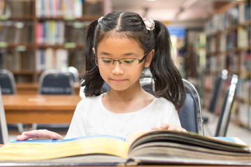 School education and literacy concept with Asian girl kid student learning and reading book in library or classroom