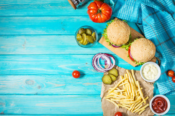 Two beef burgers, fries potatoes and cucumber on blue wood table