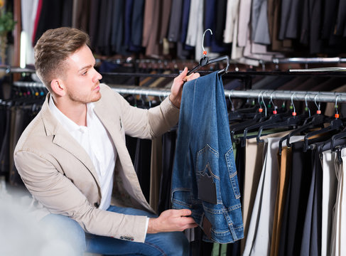 male customer examining trousers in men’s cloths store
