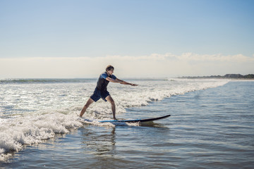 Young man, beginner Surfer learns to surf on a sea foam on the Bali island