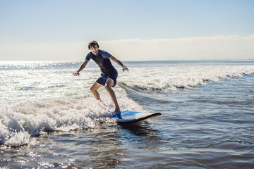 Fototapeta na wymiar Young man, beginner Surfer learns to surf on a sea foam on the Bali island