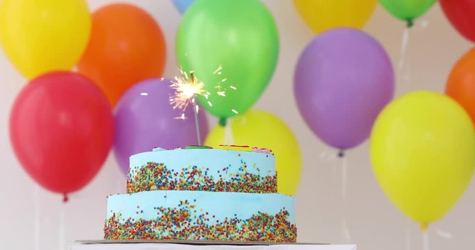 Blue Birthday cake with sparkler and colorful balloons.