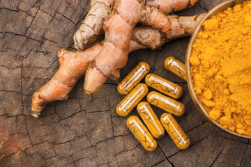 Turmeric powder in wooden bowls and turmeric capsules on wooden background