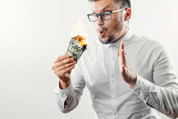A man holds burning money in his hands, burning US dollars. The concept of inflation, a decrease in...